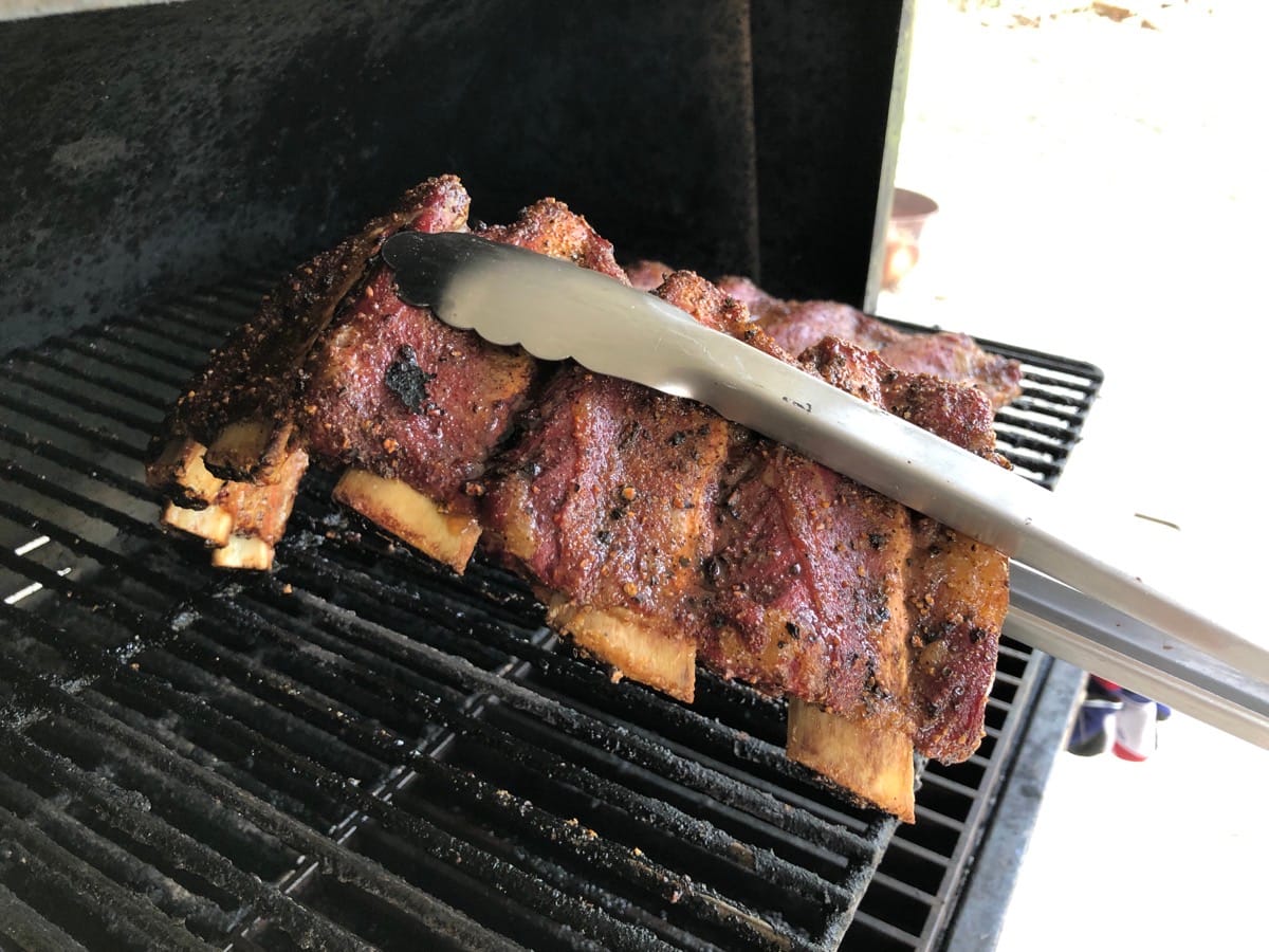 Rendered beef finger ribs being pulled off our MAK 2 Star pellet grill with our Oxo 16” Tongs