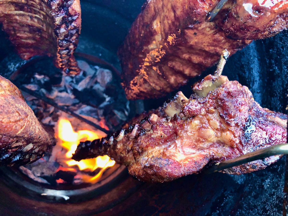 Meat pulled up on the bone on baby back ribs hanging over a live fire on the Pit barrel Cooker. One of the most beautiful views you will ever see!
