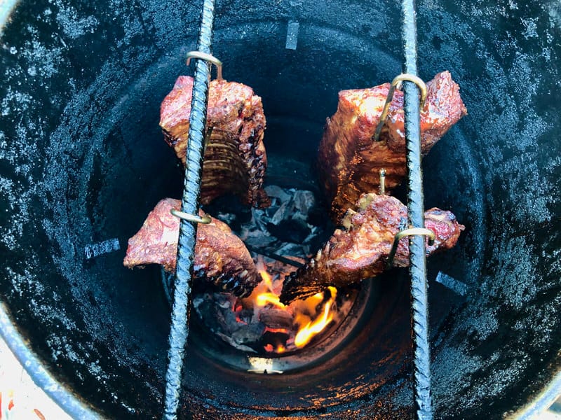 Baby back ribs hanging over live fire on The Pit Barrel Cooker.