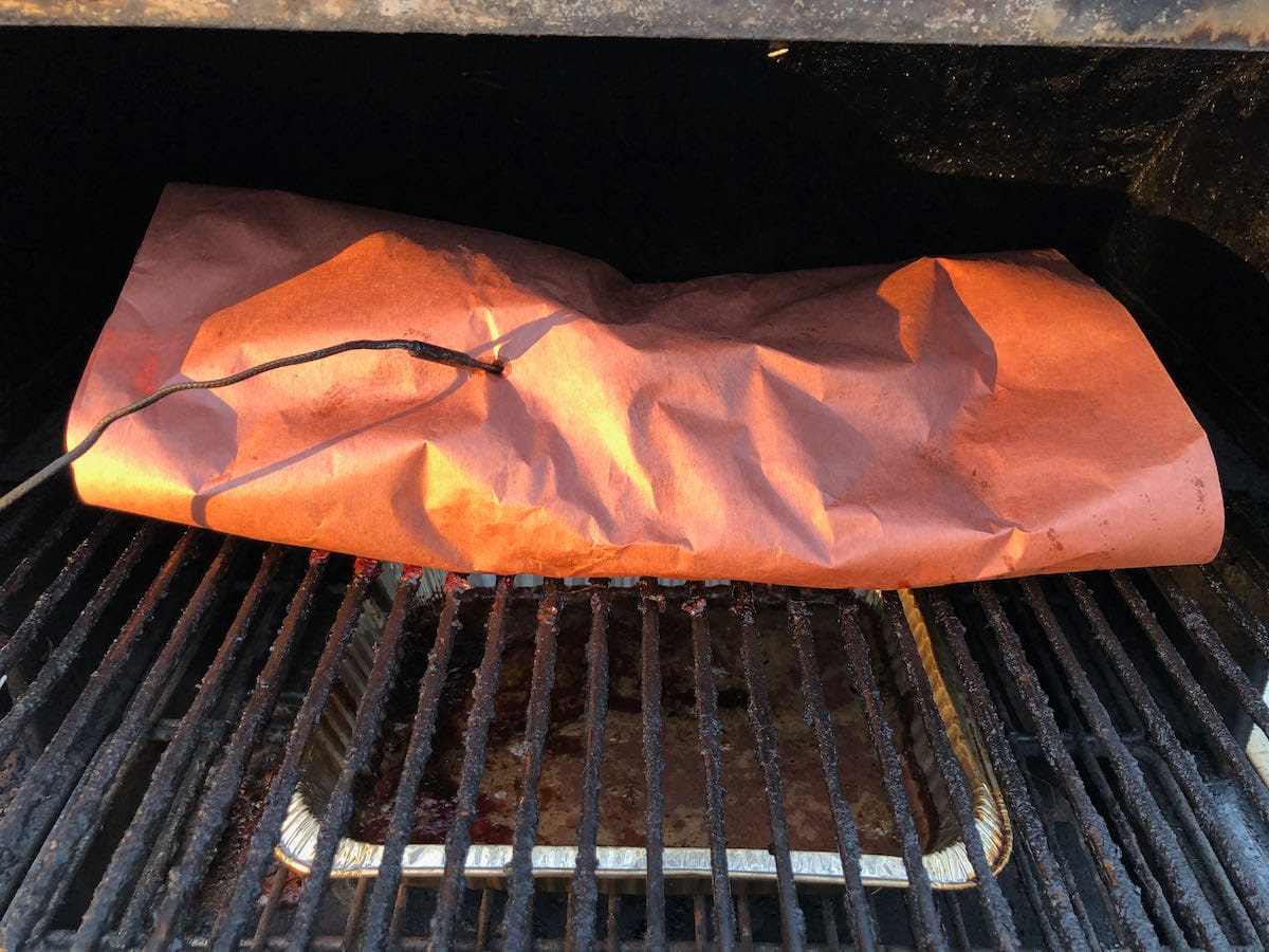 Piedmontese brisket wrapped in butcher paper on MAK 2 Star pellet grill upper rack. Pellet Boss controller temperature probe is inserted.