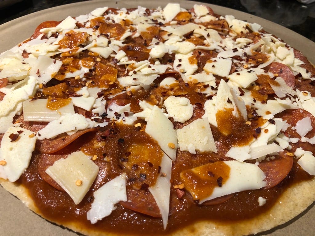 First pizza prepared with sauce, pepperoni, shaved parmesan, garlic powder, and red pepper flakes